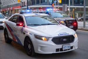 A police car with lights on, driving down the street, enforcing the Provincial Offences Act.